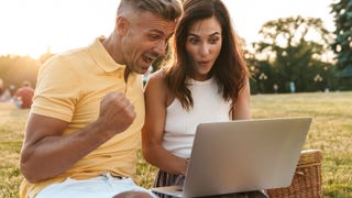 A ridiculous photograph of two middle-aged people sitting in a park and getting very excited about whatever it is they're looking at on a laptop.