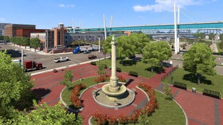 A screenshot of American Truck Simulator's Iowa expansion showing a column-like fountain in a city plaza surrounded by trees.