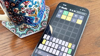 A photo of an iphone and cup of coffee on a table. An in-progress game of Wordle is visible on the phone's screen.